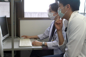 2人の医療従事者がマスクを着用し、コンピューター画面を見ながら会話をしている様子。