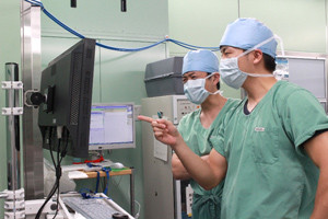 医療用スクラブを着た二人の医療従事者が、手術室でモニターを見ながら話している様子。