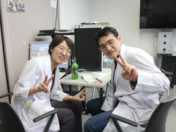 白衣を着た二人が笑顔を見せながらピースサインをしている様子。