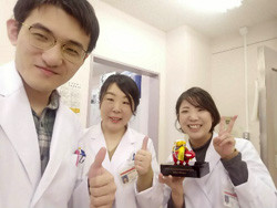 白衣を着た3人が親指を立ててポーズをとっている様子。