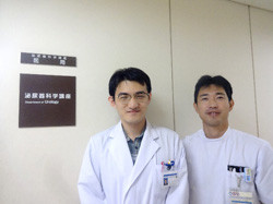 白衣を着た二人が、泌尿器科学講座の看板の前で並んで立っている。