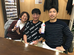 3人の人々がボトルを持ちながら座って微笑んでいます。