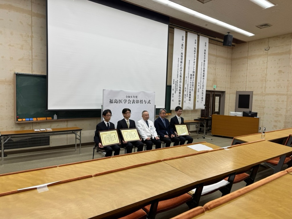三村耕作准教授が福島医学賞を受賞し、表彰式で賞状を持つ姿が映る教室の様子。