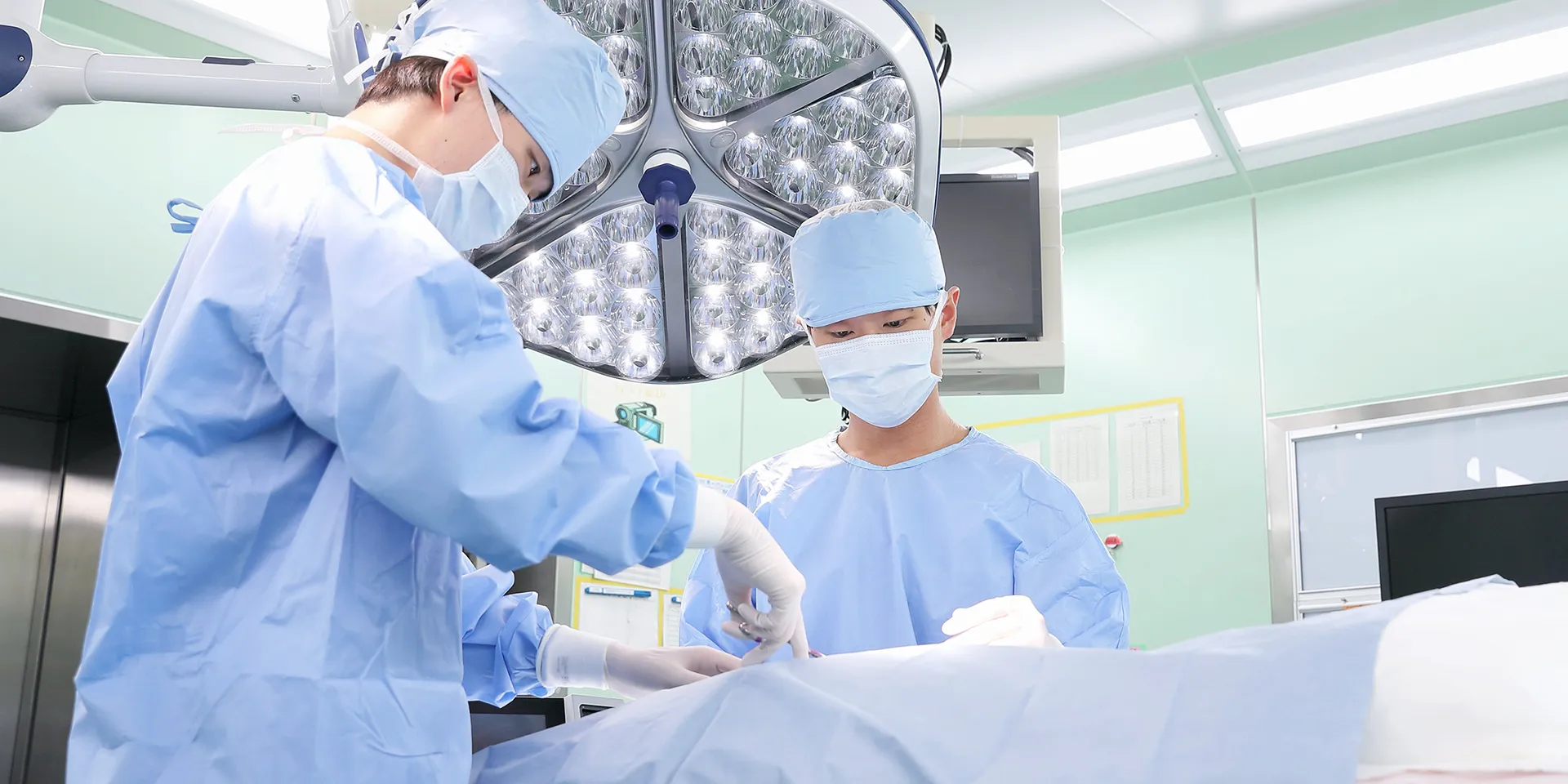 手術室で青い手術着を着た医師が患者の手術を行っている様子。明るい手術用照明が照らす中、集中している表情。