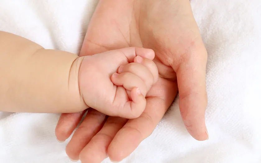 赤ちゃんの小さな手が大人の手を優しく握っている様子。温かい触れ合いを表現。