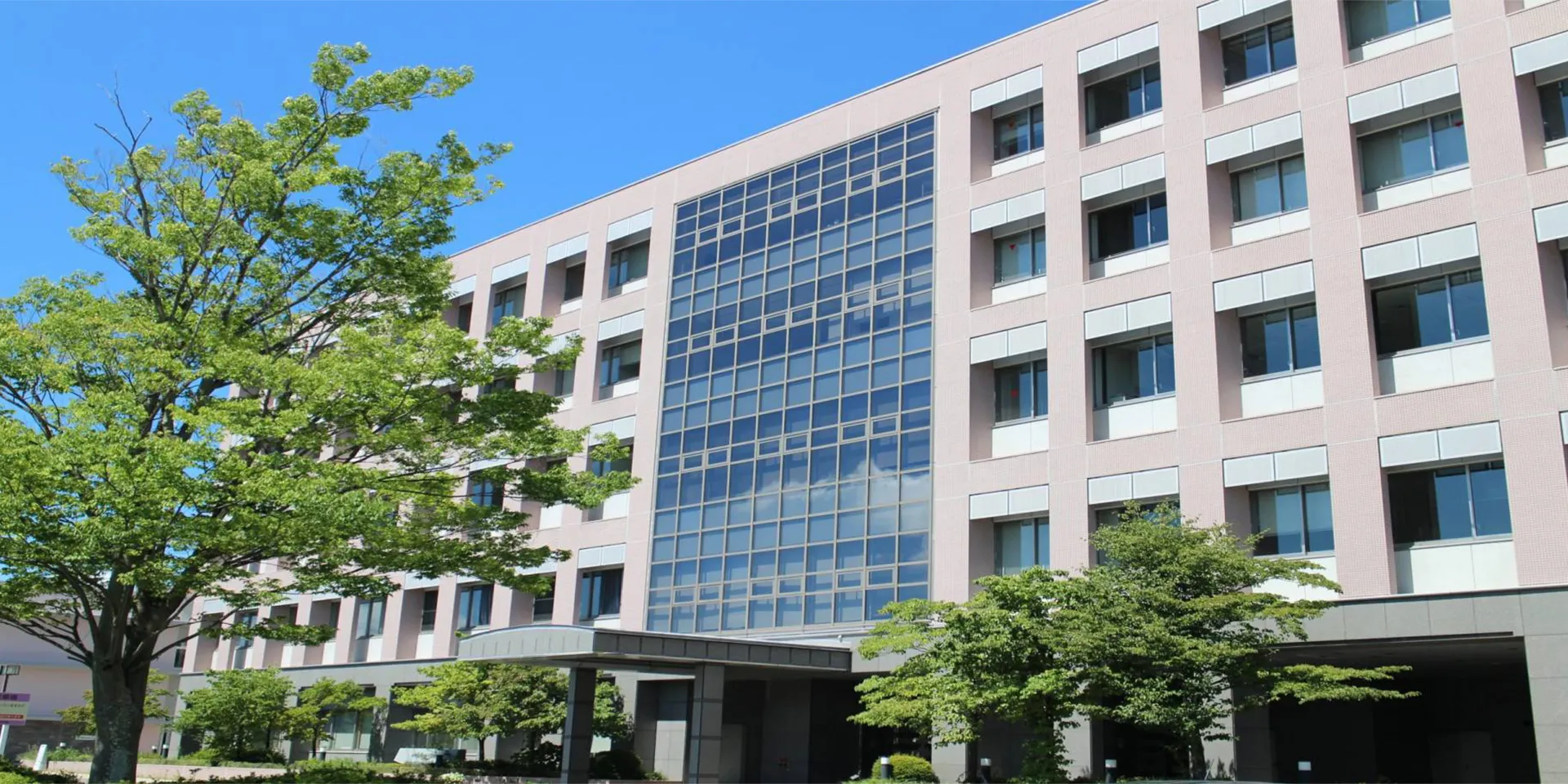 福島県立医科大学の建物と周囲の緑豊かな木々が映る晴れた日の風景。