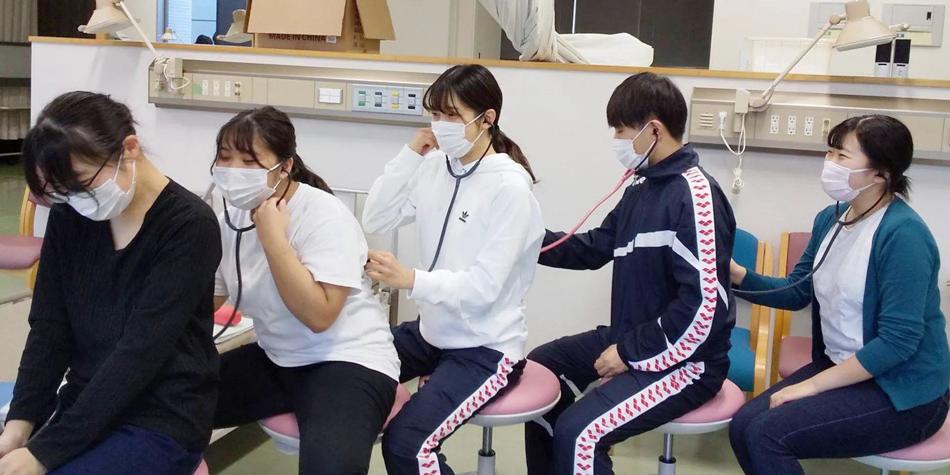 看護学部の学生が聴診器を使って互いに健康チェックを行っている様子。