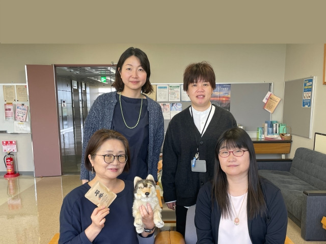 老年看護学領域の教員4人が集まり、犬のぬいぐるみを持って笑顔でポーズをとっている様子。
