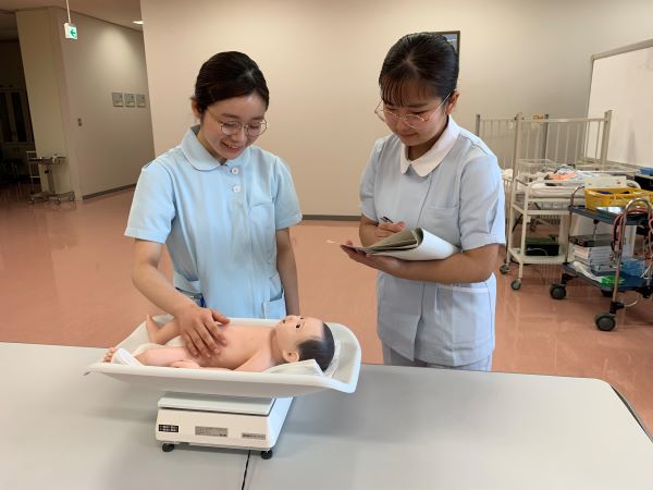 小児看護学の授業で、学生が人形の赤ちゃんを測定しながら学んでいる様子。