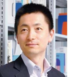福島県立医科大学の教授、三澤文紀氏が書棚の前で微笑んでいるポートレート。