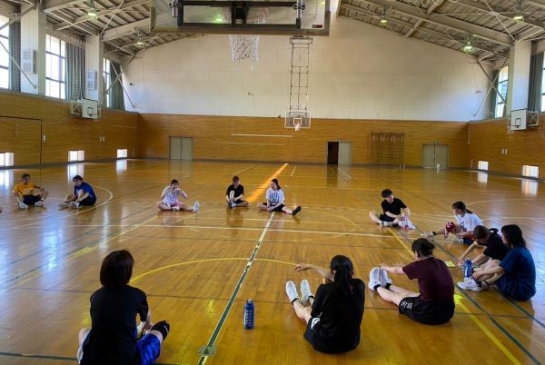 女子バスケットボール部のメンバーが練習前後に円になってストレッチを行い、楽しくおしゃべりしながらけが予防をしています。