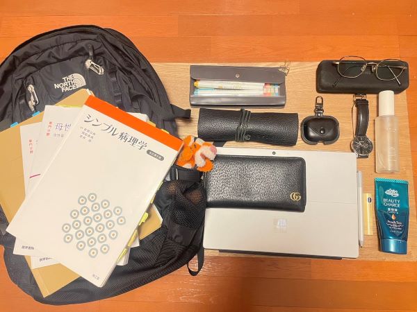 黒いリュックの中に文房具や教科書、ノートパソコン、眼鏡、時計などが整然と並べられている様子。