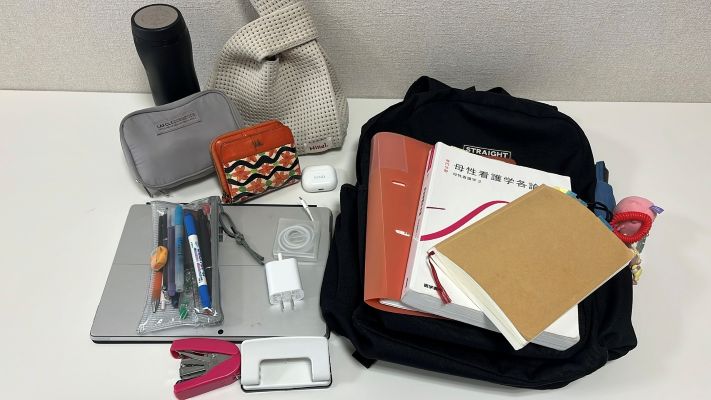 机上に黒いバックパック、教科書・ノート・ペンケース・文房具・充電器などが並ぶ。