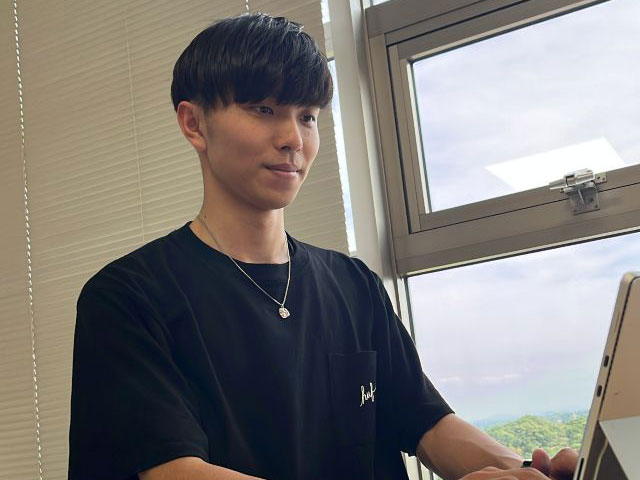 若い男性が教室の窓際でパソコンを使っている様子。