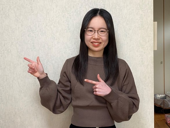 在校生が笑顔で指を指しながらポーズをとっている写真。背景はシンプルな壁。