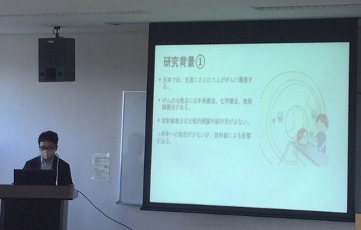 看護研究計画書発表会でプレゼンテーションを行う男性と、スライドに表示された研究背景の内容。