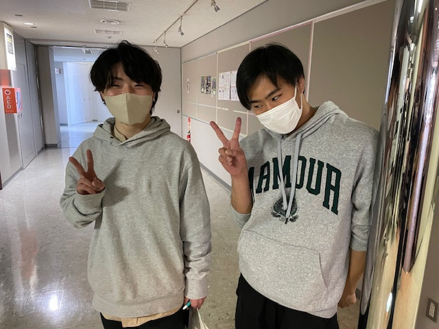 就職ガイダンス後に笑顔でピースサインをする2人の学生。