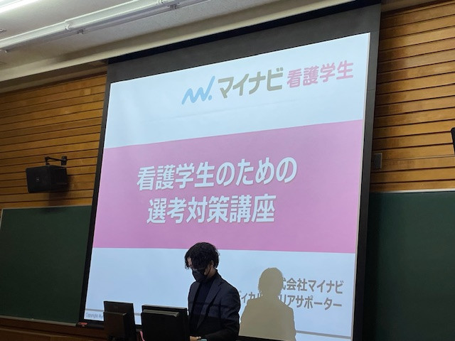 就職セミナーで講師がプレゼンテーションを行っている様子。背景には「看護学生のための選考対策講座」のスライドが映し出されている。
