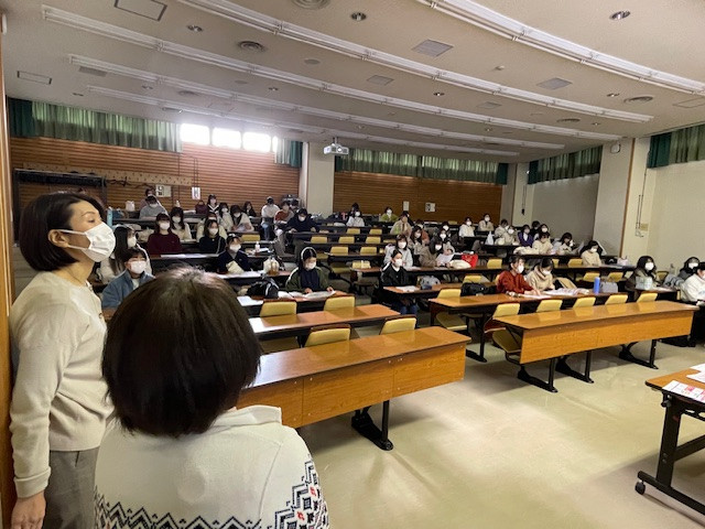 就職セミナーの会場で、マスクを着用した参加者が座っている様子。前方には講師が立っている。