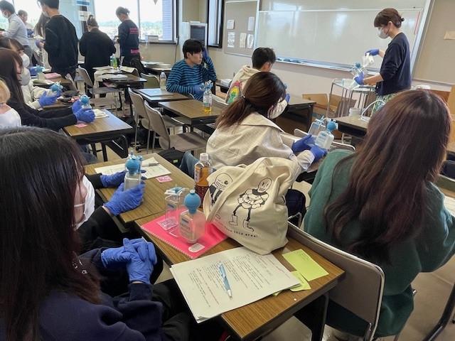 看護学部の教室で、ドレーン管理について真剣に学ぶ学生たちの様子。