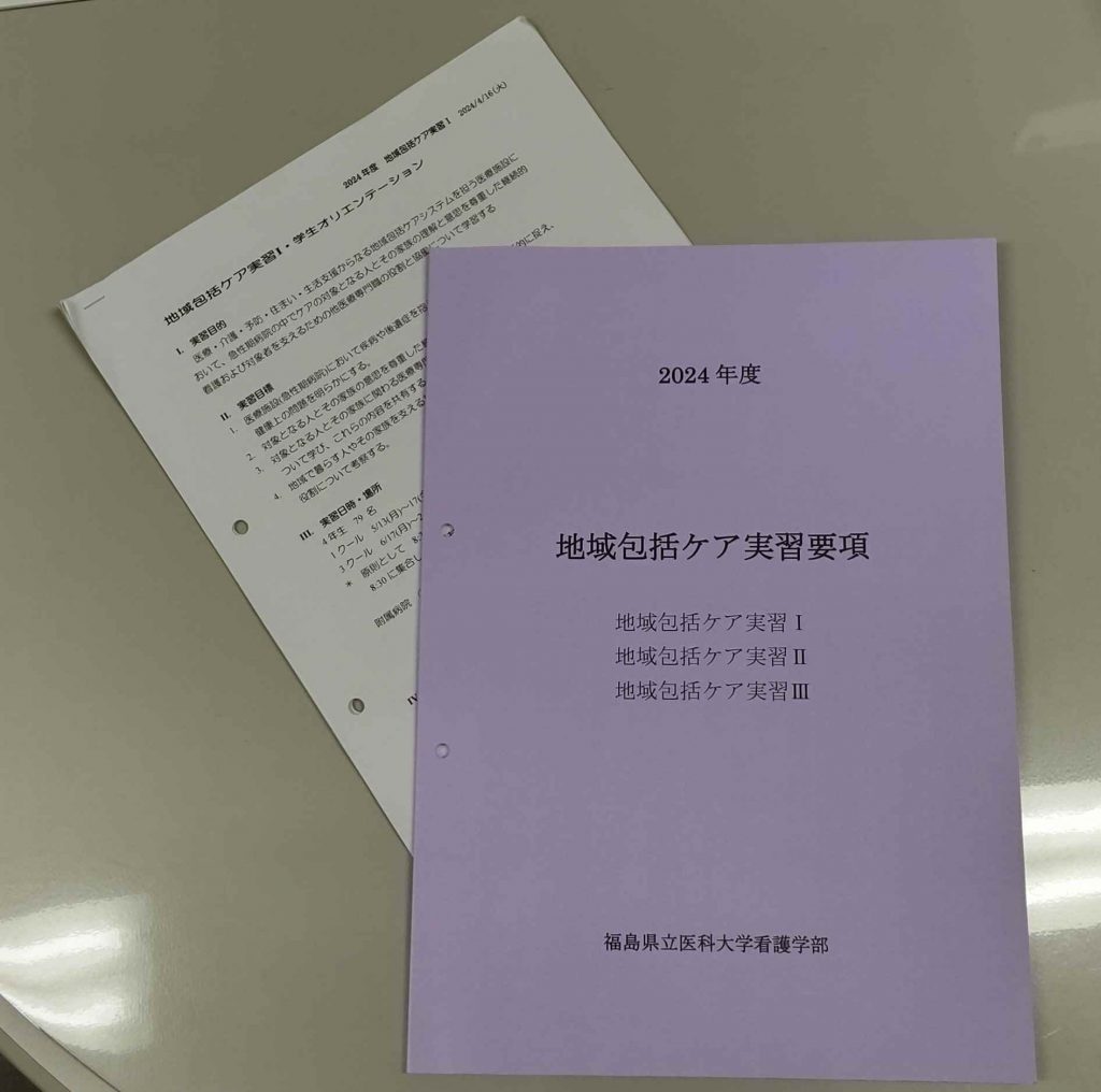 地域包括ケア実習に関する資料が置かれた机の上の写真。紫色の表紙の冊子と白い書類が写っている。