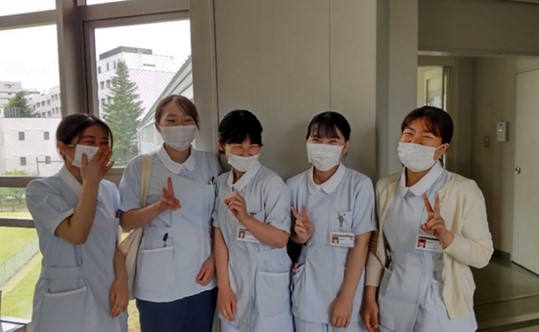 明るい表情でポーズをとる看護学生5名が、実習に向かう前の様子を捉えた写真。