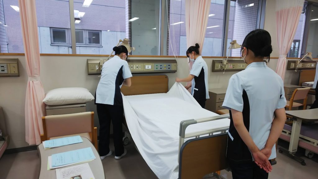 看護学生がベッドメーキングを実践している様子。病室内でシーツを整えている。