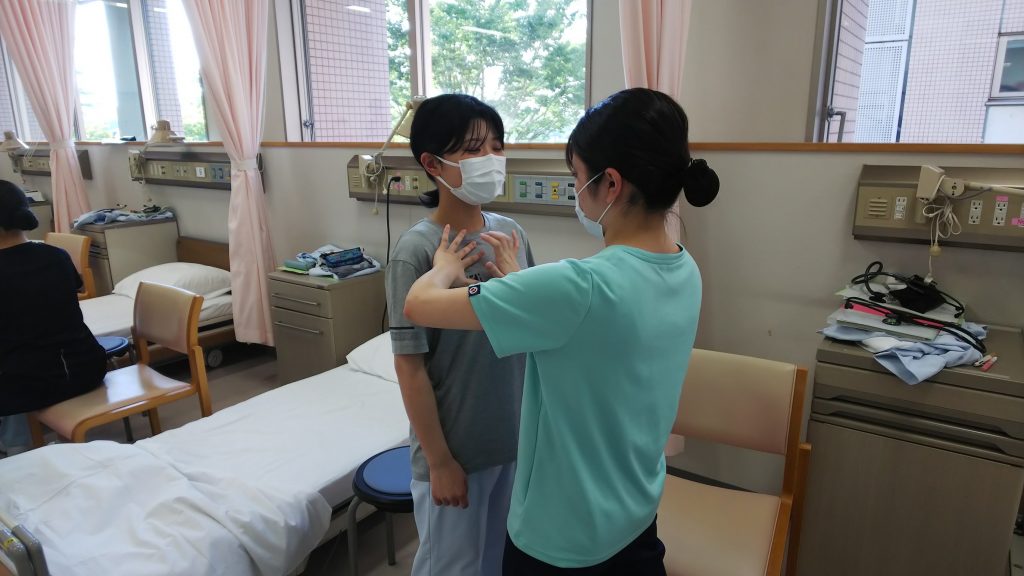 看護技術の実習中、学生が患者に対して打診を行っている様子。