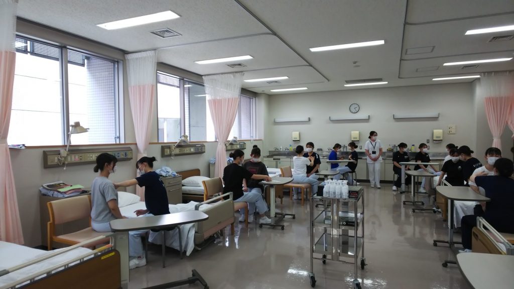 看護技術の授業中、学生たちが打診や聴診の練習を行っている教室の様子。