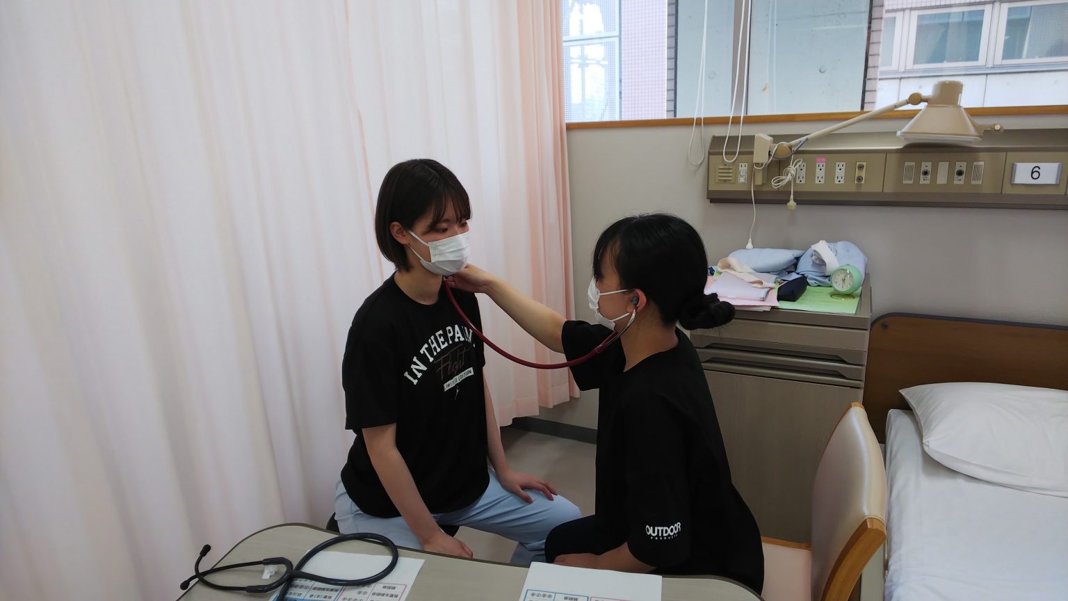 看護技術の実習中、学生が聴診器を使って患者の心音を確認している様子。