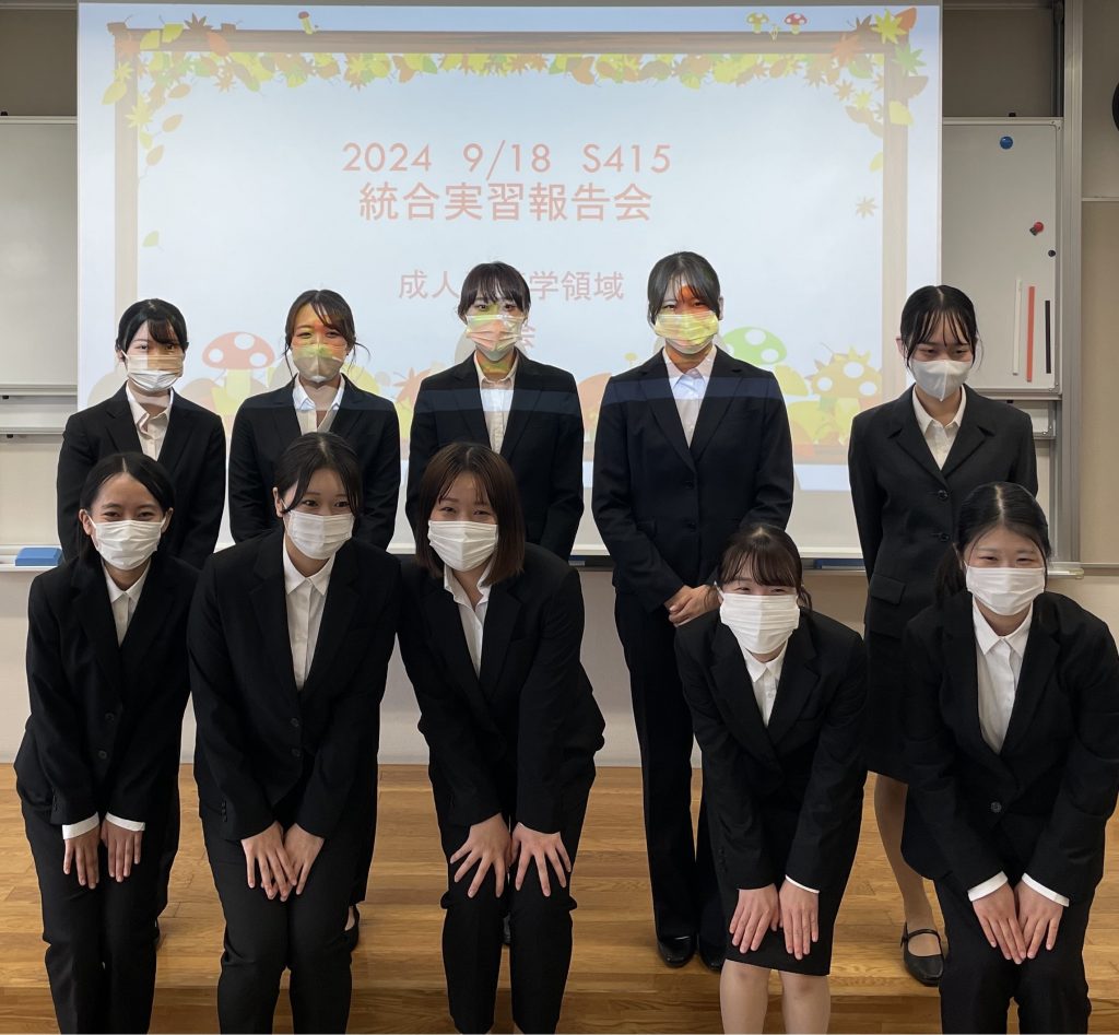 2024年度統合実習報告会に参加した学生たちが、スーツを着てポーズをとっている写真。背景には発表タイトルが表示されている。
