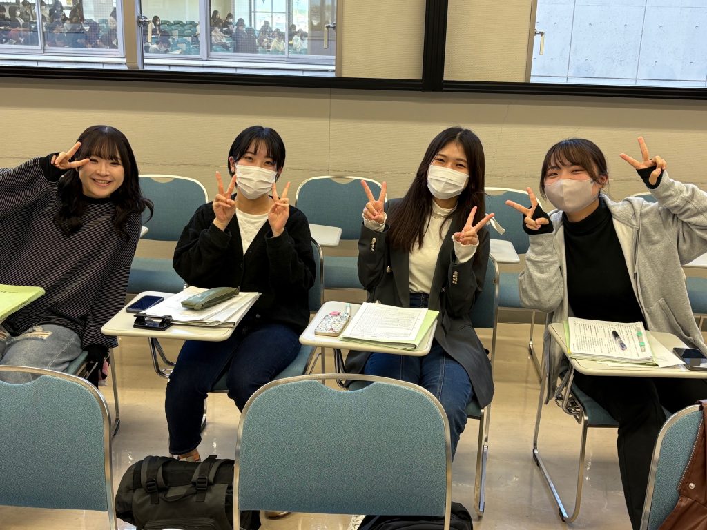 看護実習を終えた学生たちが、教室で笑顔でピースサインをしている様子。