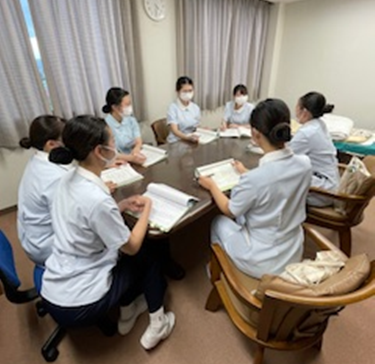看護学生たちがあづま脳神経外科病院で実習のために集まり、テーブルを囲んで学習している様子。