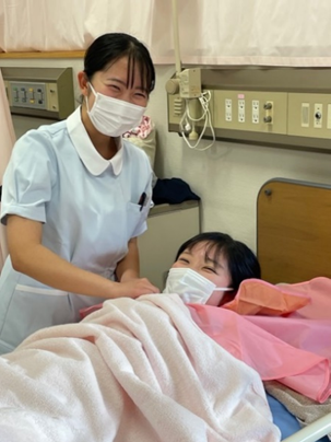 看護技術の演習で洗髪を行う学生と患者の様子。学生はマスクを着用し、患者に優しく接している。