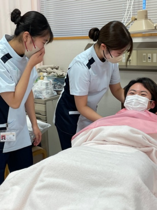 看護技術の演習で洗髪を行う学生たちが、患者に寄り添いながらサポートしている様子。