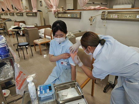 看護学生が筋肉内注射の演習を受けている様子。注射を受ける学生は緊張した表情を見せている。