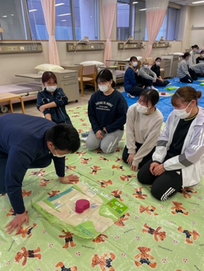 看護技術の演習で救命救急処置を学ぶ学生たちが、実習用マットの上で指導を受けている様子。