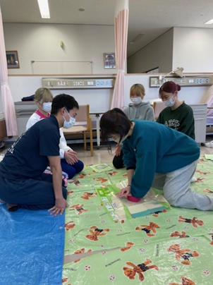 看護技術の演習で救命救急処置を学ぶ学生たちが、マットの上で実技を行っている様子。