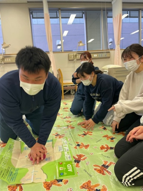 看護技術の演習で心肺蘇生法を学ぶ学生たちが、マットの上で実践している様子。