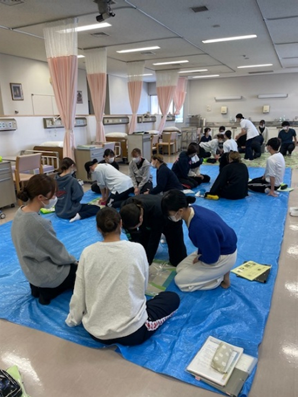 看護技術の演習で救命救急処置を学ぶ学生たちが、青いシートの上で実習を行っている様子。