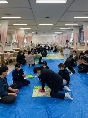 看護技術の演習で救命救急処置を学ぶ学生たちが、青いシートの上で実習を行っている様子。
