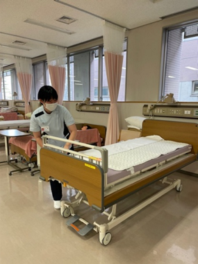 看護学生が病室でベッドメイキングを行っている様子。ボディメカニクスを意識して作業中。