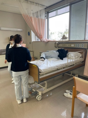 患者が寝ているベッドのそばで、看護学生がシーツ交換を行っている様子。