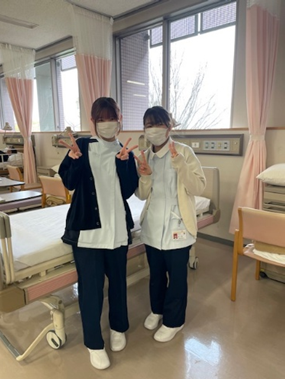 看護技術を学ぶ学生が病院の実習室で笑顔でポーズをとっているオフショット。