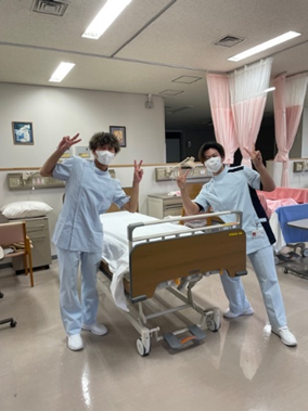 看護技術の自己学習を行う福島県立医科大学の1年生が、病室で笑顔でポーズをとっている様子。
