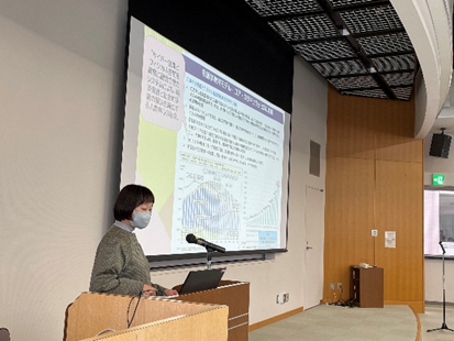 2024年度臨地実習教育会議の全体会で発表を行う女性講師とプロジェクターのスライド。