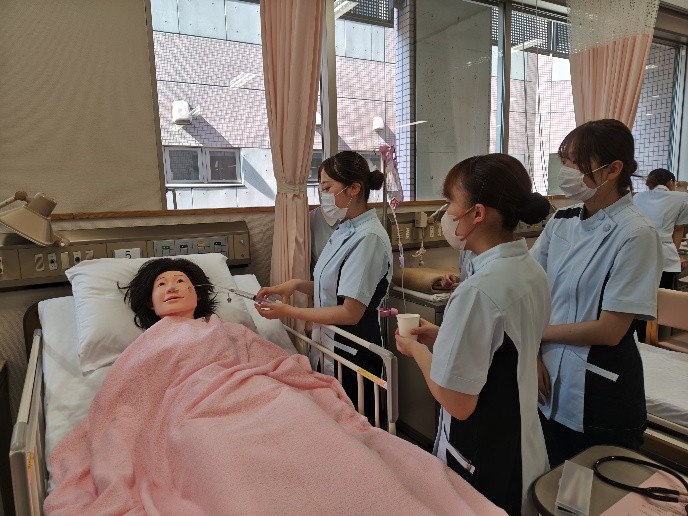 看護技術の演習で、経管栄養を行う学生たちが人形に白湯を注入している様子。