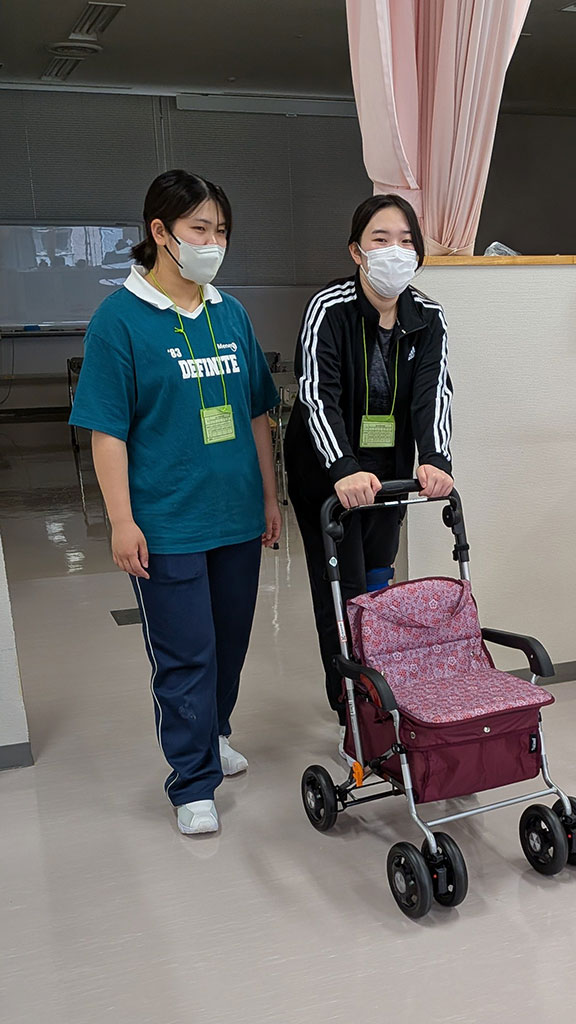 高齢者の疑似体験を行う学生たちが、食事介助用のカートを押している様子。