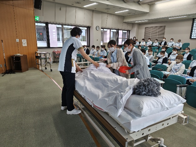 看護技術の演習で、学生たちが体温管理のために湯たんぽや毛布を使っている様子。