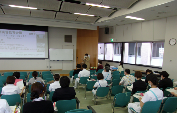 2022年度「臨地実習教育会議」の全体会で、講演を行う講師と参加者の様子。